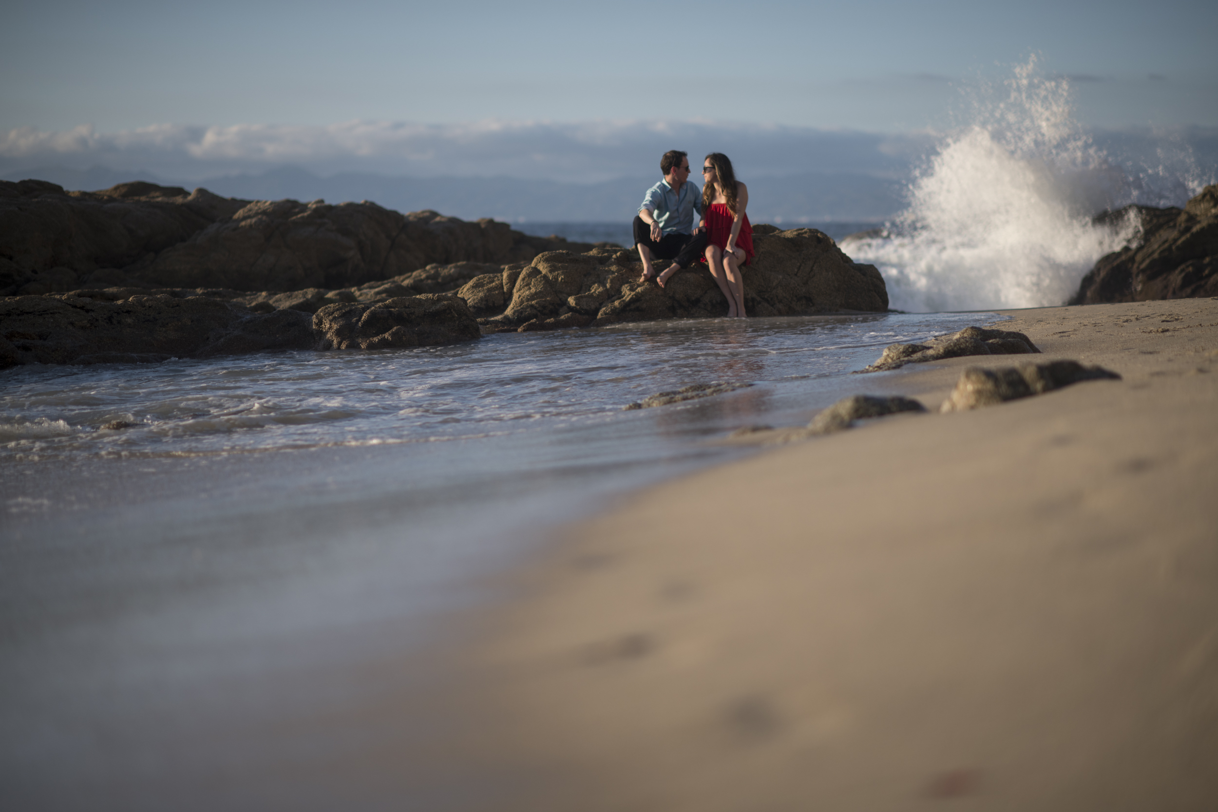 Pareja comprometida en las rocas mientras rompe una ola, Puerto Vallarta