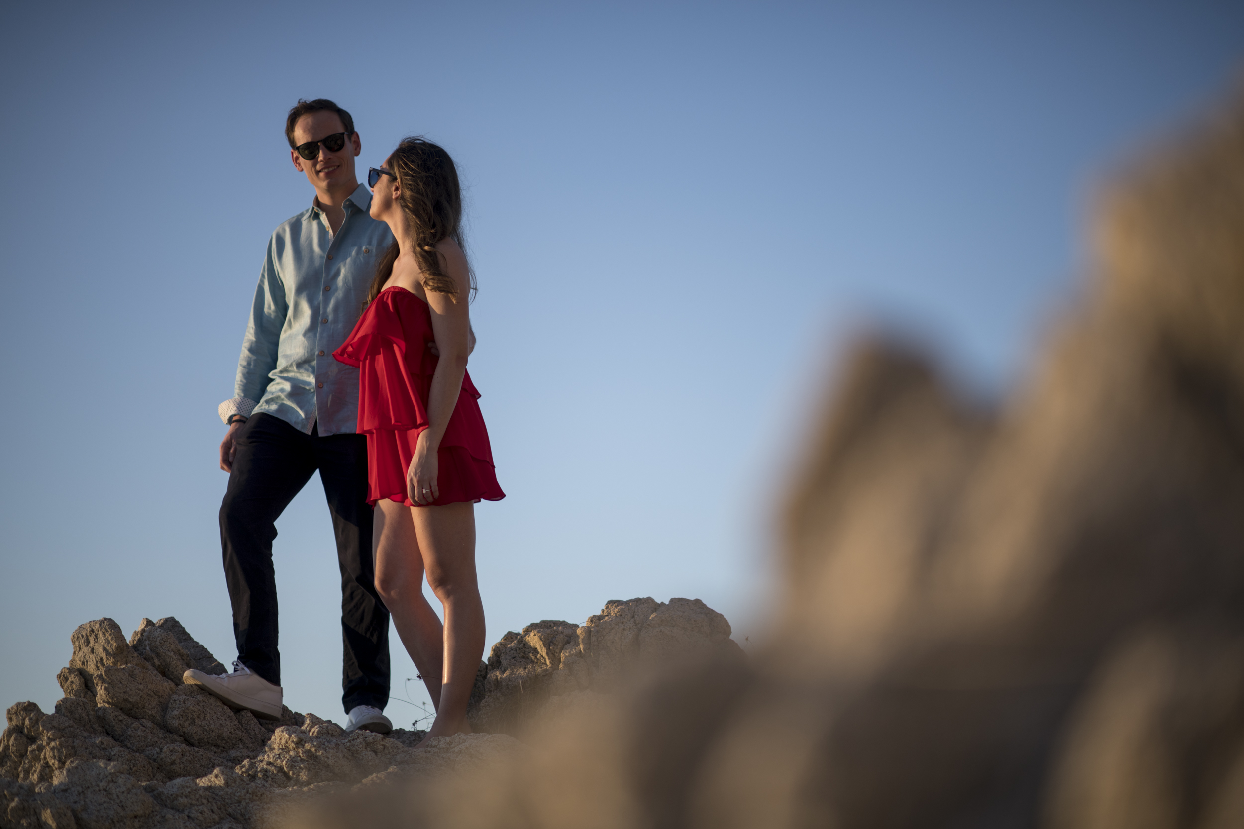 Pareja comprometida de pie sobre las rocas al atardecer, Conchas Chinas