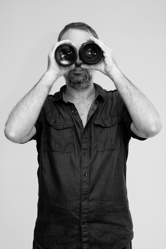 Julien — photographer, looking through two camera lenses like binoculars